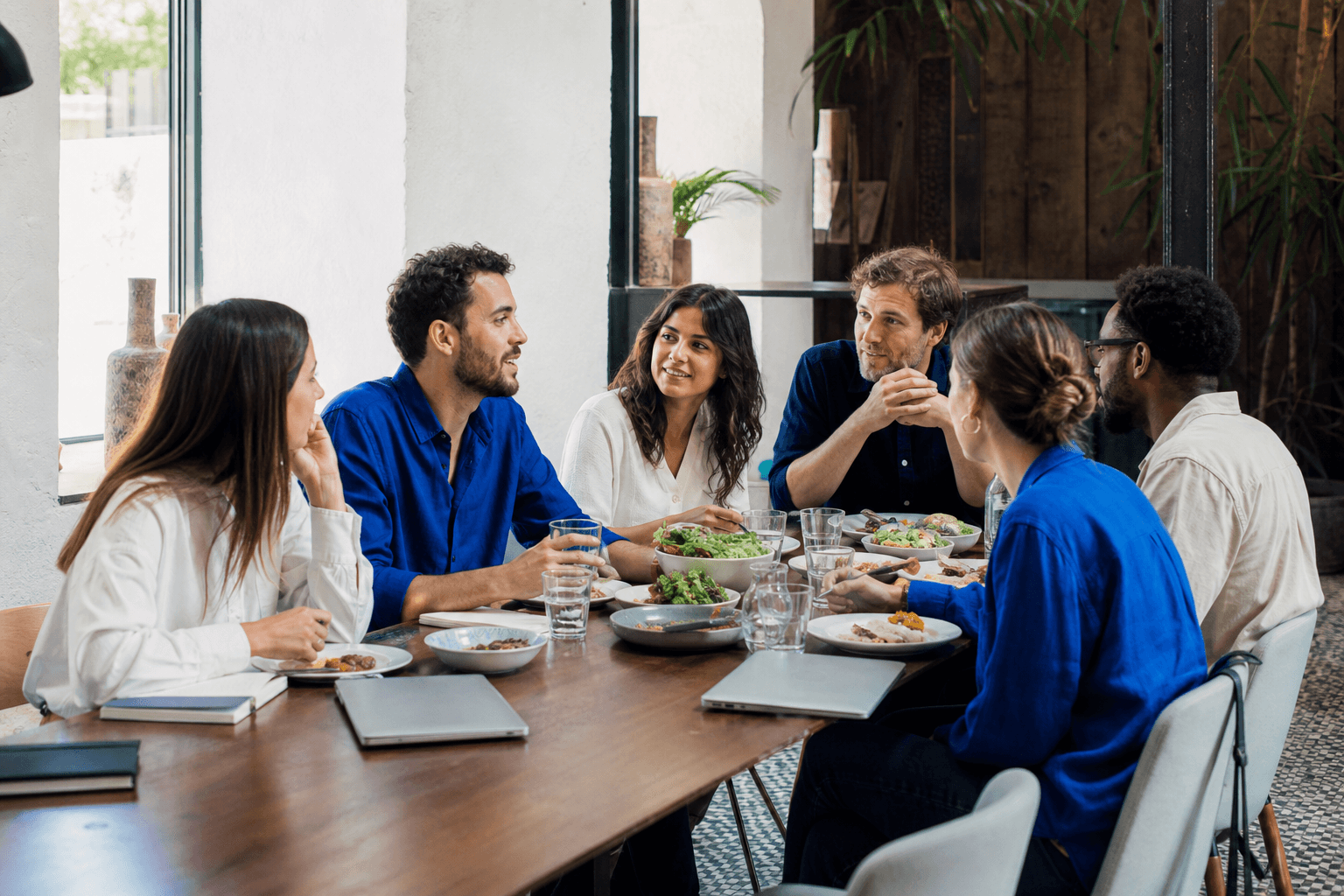 Six remote workers sharing lunch around a table with their laptops nearby